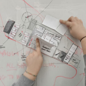 a woman's hands with a pencil over an architectural plan on a desk.