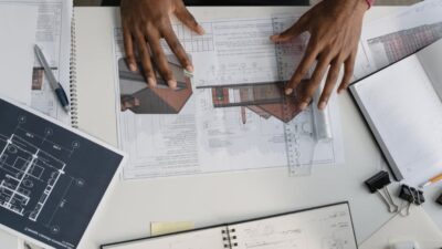 Overhead view of hands working on architectural plans with a ruler and a pen on the paperwork