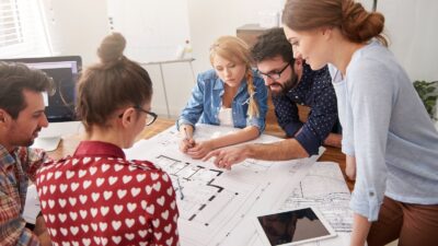 Coworkers at office with architecture plans and a computer